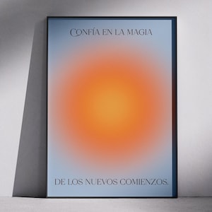 May include: Framed art print with a gradient design. The artwork features a central orange and yellow orb against a light blue background. The text "CONFÍA EN LA MAGIA" and "DE LOS NUEVOS COMIENZOS" are printed in black.