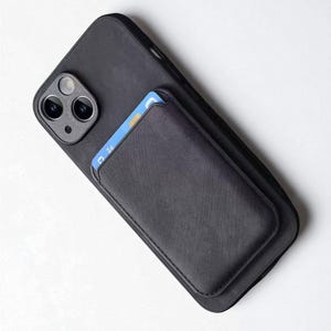 Op de afbeelding: Zwarte telefoonhoes met een ingebouwde kaarthouder. De hoes is gemaakt van een textuurrijk materiaal en heeft een ontwerp met dubbele camera. Een blauw-witte kaart is gedeeltelijk zichtbaar in de kaarthouder.