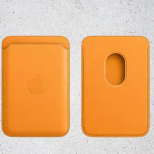 May include: Two orange leather card holders. The front of one has an embossed Apple logo. The back of the other has an oval cutout. Both have stitched edges. The card holders are shown against a mottled gray background.