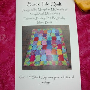 May include: A white card with the title "Stack Tile Quilt" and instructions for making a quilt. The quilt is made with 10 inch stack squares and features a colorful paisley pattern.