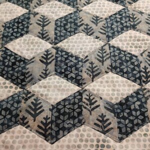 May include: A quilt with a geometric pattern of white, gray, and blue squares and diamonds. The squares have a repeating pattern of small white dots, while the diamonds have a repeating pattern of stylized trees and snowflakes.
