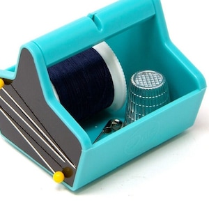 May include: A turquoise plastic sewing kit shaped like a toolbox with a spool of navy blue thread, a thimble, a safety pin, and several needles.