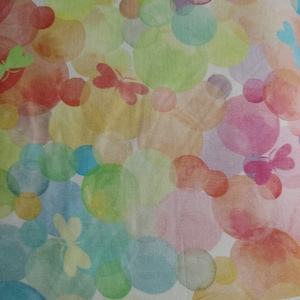 May include: A white fabric with a colorful watercolor pattern of overlapping circles and butterflies. The fabric has the text "tamarak by" printed on it.