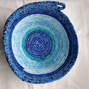 Pode incluir: Uma tigela de tecido azul e branco com uma alça de corda. A tigela é feita de tecido enrolado e tem um padrão azul e branco.