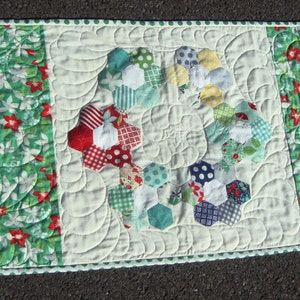 Peut inclure: Un chemin de table blanc avec un motif floral vert sur les côtés et un motif patchwork coloré au centre. Le motif patchwork présente un cercle d'hexagones de différentes couleurs et motifs.