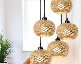 May include: Five woven wicker pendant lights hang from the ceiling in a stairwell. The lights are round and have a natural, light brown color. The lights are hanging from black cords.
