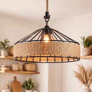 Może przedstawiać: Rustykalna lampa wisząca z tkanym, beżowym kloszem i czarną metalową ramą wisi na grubym sznurze. Oprawa oświetla kuchnię z drewnianymi półkami, roślinami i blatem z tkanym koszem.