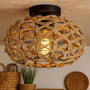 May include: An oval-shaped ceiling light fixture with a woven rope design. The light is encased in a black metal frame and has a warm, yellow glow. The fixture is mounted on a wooden ceiling. The overall style is rustic and natural.