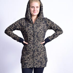 May include: A hooded zip-up jacket with a unique pattern in shades of black and tan. The jacket features a full-length zipper, long sleeves, and a hood. The model is wearing black leggings and black fingerless gloves.