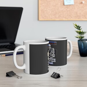 Puede incluir: Taza de café de cerámica blanca con un gráfico negro de un esqueleto trabajando en una computadora. El texto en la taza dice "meeting and have email". La taza está sobre una superficie clara, con un portátil y material de oficina en el fondo.