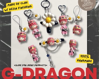 May include: Handmade clay figurines with resin finishing, featuring a G-Dragon theme. The collection includes keychains, earrings, and a hair accessory, all adorned with miniature figures and daisy accents. The text "100% Handmade" is visible.