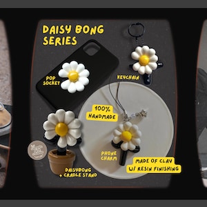 Puede incluir: Una colecci&oacute;n de accesorios hechos a mano con tem&aacute;tica de margaritas, que incluyen un soporte para tel&eacute;fono, un llavero, un dije para tel&eacute;fono y un daisy bong con un soporte. Los art&iacute;culos son blancos y amarillos con detalles en negro, hechos de arcilla con acabado de resina.