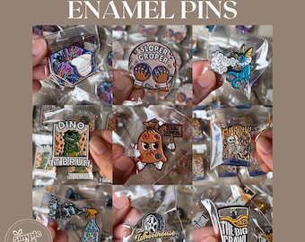 May include: A collection of custom enamel pins in clear plastic packaging. The pins feature various designs, including a dinosaur, a skeleton, and text that reads "SLOPER GROPER" and "THE BIG CRAWL". The pins are colorful and detailed.