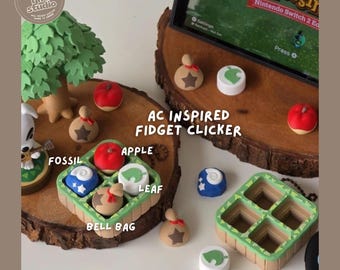 May include: A set of AC inspired fidget clickers featuring small, colorful game-themed tokens including a red apple, a blue fossil, a white leaf, and a tan bell bag. The set includes a square green grid tray and individual pieces.