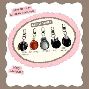 May include: Handmade Ghibli Series keychains featuring characters Susu Watari, Calcifer, Totoro, Jiji, and Kao Nashi. Each keychain is made of clay with resin finishing and includes a silver-colored clasp. The keychains are displayed on a pink oval frame.