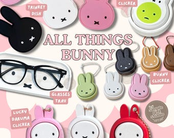 May include: A collection of bunny-themed accessories including trinket dishes, glasses trays, and clickers. The items feature Miffy-style rabbit faces in various colors like pink, white, black, green, and red. Some clickers include Japanese kanji characters.