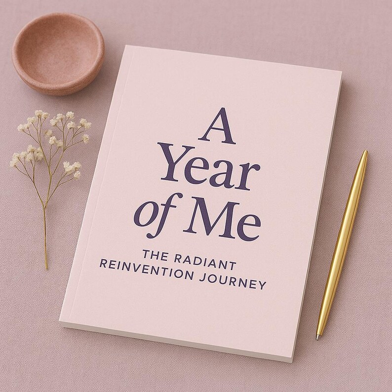 K&ouml;nnte beinhalten: Ein "A Year of Me"-Journal mit dem Untertitel "The Radiant Reinvention Journey" in dunkelblauem Text auf einem hellrosa Einband. Ein goldener Stift liegt neben dem Journal, mit einer kleinen rosa Schale und einem Zweig wei&szlig;er Blumen.