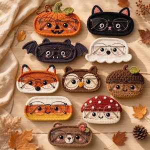 May include: A collection of ten crocheted eyeglass cases shaped like various characters including a pumpkin, black cat, bat, ghost, fox, owl, acorn, candy corn, mushroom, and bear, each holding a pair of thin-framed metal eyeglasses.