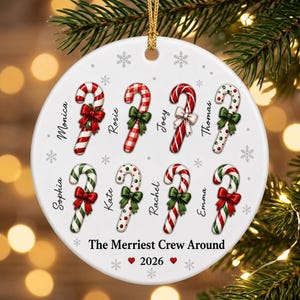 May include: A round white ceramic Christmas ornament featuring eight candy canes with red and green bows, each labelled with names including Monica, Rosie, Joey, Thomas, Sophia, Kate, Rachel, and Emma. Text reads The Merriest Crew Around 2026.