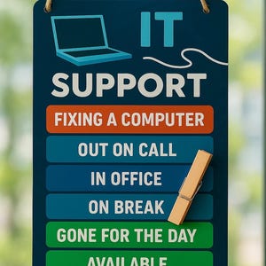 May include: A navy blue sign with the words "IT SUPPORT" and a laptop graphic. Below, it lists the IT support status: "FIXING A COMPUTER", "OUT ON CALL", "IN OFFICE", "ON BREAK", "GONE FOR THE DAY", and "AVAILABLE". A wooden clothespin is attached.