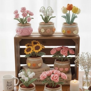 May include: A selection of handmade crochet flower pots. The pots showcase diverse floral designs, such as pink roses, yellow sunflowers, and white lilies. The pots are arranged on a wooden crate and table, creating a charming, handcrafted aesthetic.