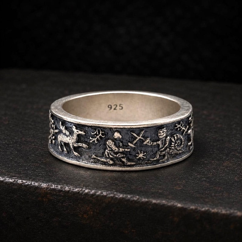 May include: A silver ring with a dark, oxidized finish featuring embossed figures of a knight, a snail, and a deer. The interior of the band is clearly stamped with the number 925, indicating the sterling silver composition of the jewelry piece.