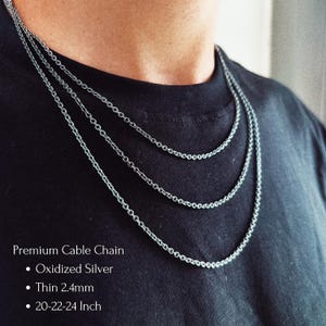 May include: Three layered oxidized silver cable chains resting against a black shirt. The text reads: Premium Cable Chain, Oxidized Silver, Thin 2.4mm, 20-22-24 Inch. The chains feature a classic interlocking link design with a dark metallic finish.