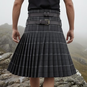 May include: A grey plaid kilt with a pleated design and two leather belts. The kilt features a classic tartan pattern with white and grey lines. The belts are dark brown with silver buckles. The kilt is worn outdoors.