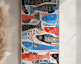 May include: A framed art print featuring a colorful illustration of sardines. The artwork showcases stylized fish in shades of blue, red, and black against a white background. The word "SARDINES" is printed on the artwork.
