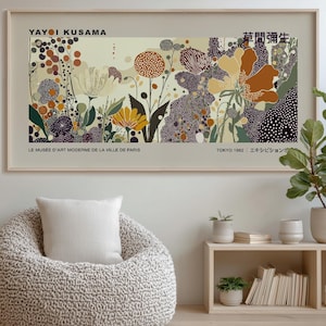 Könnte beinhalten: Ein gerahmter Kunstdruck mit einem floralen Design und einem beigen Hintergrund. Das Kunstwerk enthält den Text "YAYOI KUSAMA" und japanische Schriftzeichen. Der Druck wird über einem beigen Sitzsack und einem kleinen Holzregal angezeigt.