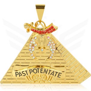 以下が含まれることがあります： 「PAST POTENTATE」の文字が入ったピラミッドデザインのゴールドカラーのペンダント。ペンダントにはゴールドのベイルが付いており、赤と虹色の宝石が飾られています。ピラミッドはレンガ模様です。