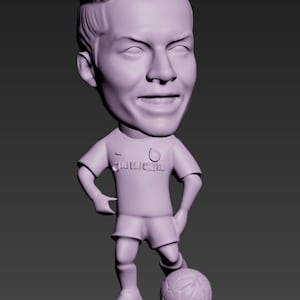 Puede incluir: Figura de futbolista con cabeza oscilante de color púrpura claro. La figura lleva una camiseta y pantalones cortos, con un balón de fútbol a sus pies. La figura tiene una cara sonriente y está de pie sobre una base rectangular.