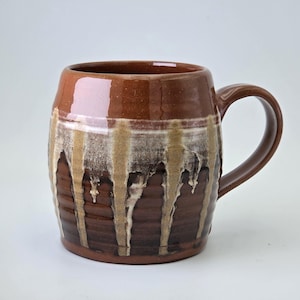 May include: A white ceramic mug with a black handle and the text "But First, Coffee" in a bold, black font. The mug is set against a blurred background, suggesting a cozy setting.