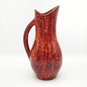 Peut inclure: Un pichet en céramique rouge avec un motif tacheté de points jaunes et verts. Le pichet a une anse incurvée et un bec évasé. L'intérieur du bec est de couleur marron clair. C'est un objet décoratif.