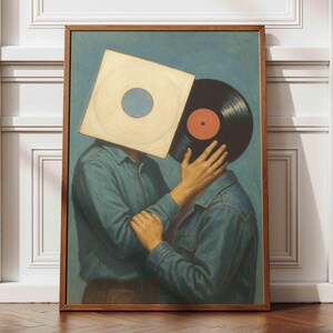 May include: A framed art print depicting two figures in denim shirts, their faces replaced by a vinyl record and its sleeve. The artwork has a vintage style, with a blue backdrop and a wooden frame. The figures are embracing, creating a romantic and artistic scene.