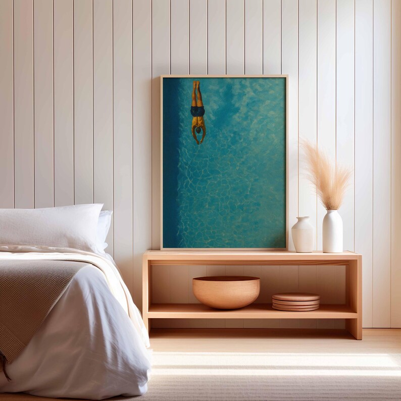May include: A framed print featuring a person diving into a turquoise pool. The image is set in a light wood frame and is displayed on a wooden shelf. Decorative vases and a wooden bowl are also on the shelf.