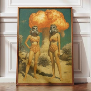 Könnte beinhalten: Gerahmter Druck mit zwei Figuren in Retro-Badebekleidung und Gasmasken vor einer großen orangefarbenen Explosion. Das Kunstwerk hat eine Vintage-Ästhetik, mit einer Wüstenlandschaft und einem Holzrahmen.