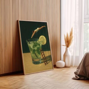 Pu&ograve; includere: Stampa artistica incorniciata raffigurante un cocktail mojito con una fetta di limone e foglie di menta. Una persona in costume da bagno bianco si tuffa nella bevanda. Una piccola scala di legno &egrave; appoggiata al bicchiere.