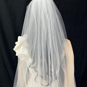 K&ouml;nnte beinhalten: Ein einlagiger Braut Schleier aus weichem T&uuml;ll mit einer gewellten Kante. Der Schleier ist so konzipiert, dass er &uuml;ber dem Kopf getragen wird.