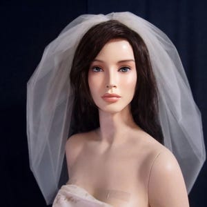 May include: A white bridal veil made of tulle, worn by a woman with long dark hair. The veil is gathered at the top and falls down the back, covering the woman's shoulders.
