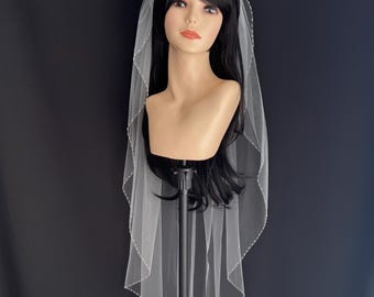 May include: A white bridal veil with a beaded edge. The veil is draped over a mannequin head with long black hair.
