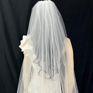K&ouml;nnte beinhalten: Ein einlagiger Braut-Schleier aus weichem T&uuml;ll mit einem gewellten Rand. Der Schleier ist so konzipiert, dass er &uuml;ber dem Kopf getragen wird.