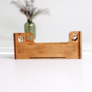 May include: A rectangular wooden pet bed frame with a light brown finish. The side panels feature cut-out paw print designs on the upper corners. The structure is composed of flat wooden boards with visible grain, designed with a low profile.