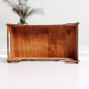 May include: A rectangular wooden tray with a medium brown stained finish. The tray features vertical side panels with integrated oval handle cutouts and decorative paw print cutouts along the bottom edges of the side panels.