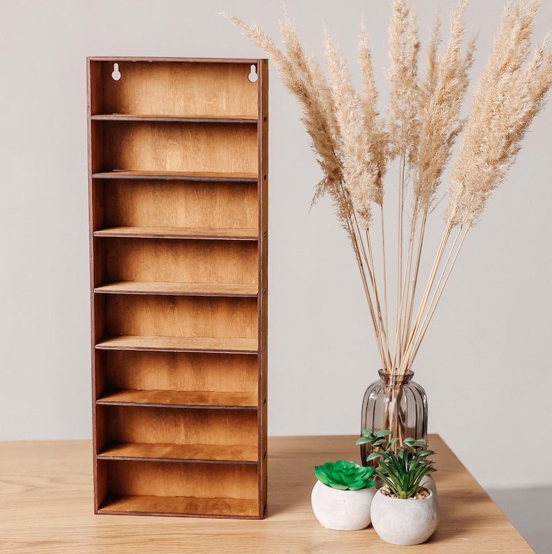May include: A tall, rectangular wooden wall shelf featuring eight horizontal storage compartments with a natural brown wood grain finish and two circular mounting holes at the top for secure installation on a vertical surface.