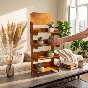 Op de afbeelding: Een houten displayplank met vier niveaus en een gladde bruine afwerking. De unit heeft vier horizontale planken, elk met een kleine vetplant in een pot. De structuur is open aan de zijkanten en heeft een hoog achterpaneel voor op tafel.