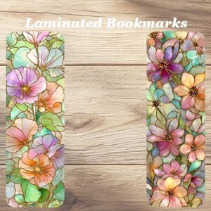 May include: Two laminated bookmarks with floral designs. The bookmarks feature colorful flowers in shades of pink, purple, orange, and yellow, with green leaves and gold outlines. The text "Laminated Bookmarks" is at the top.