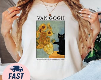 May include: Cream-colored t-shirt featuring a print of Van Gogh's "Sunflowers" painting with a black cat. The text "VAN GOGH" is above the image, and "SUNFLOWERS (THIRD VERSION) - 1888" is below. The shirt has a round neckline.