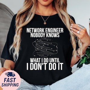 May include: Black t-shirt with white text: "NETWORK ENGINEER NOBODY KNOWS WHAT I DO UNTIL I DON'T DO IT." The shirt features a graphic of a network of lines and dots. The shirt is a crew neck.