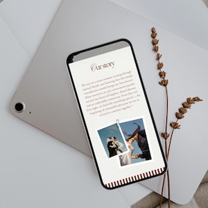 May include: A smartphone displays a wedding story with the title "Our Story" in a script font. Two photos are attached with a paper clip. The phone rests on a silver tablet and a white envelope, with dried flowers nearby.